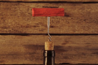 Wine bottle with corkscrew on wooden background, closeup