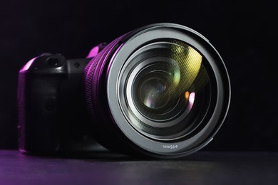 Photo of Modern photo camera on black table, closeup. Photographer's equipment