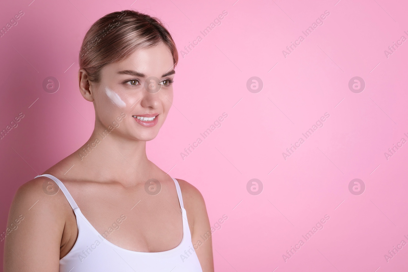 Photo of Beautiful woman with cream on her face against pink background, space for text