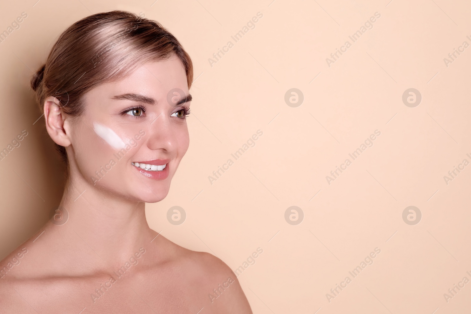 Photo of Beautiful woman with cream on her face against beige background, space for text