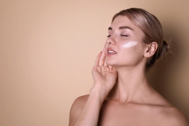 Photo of Beautiful woman with cream on her face against beige background, space for text