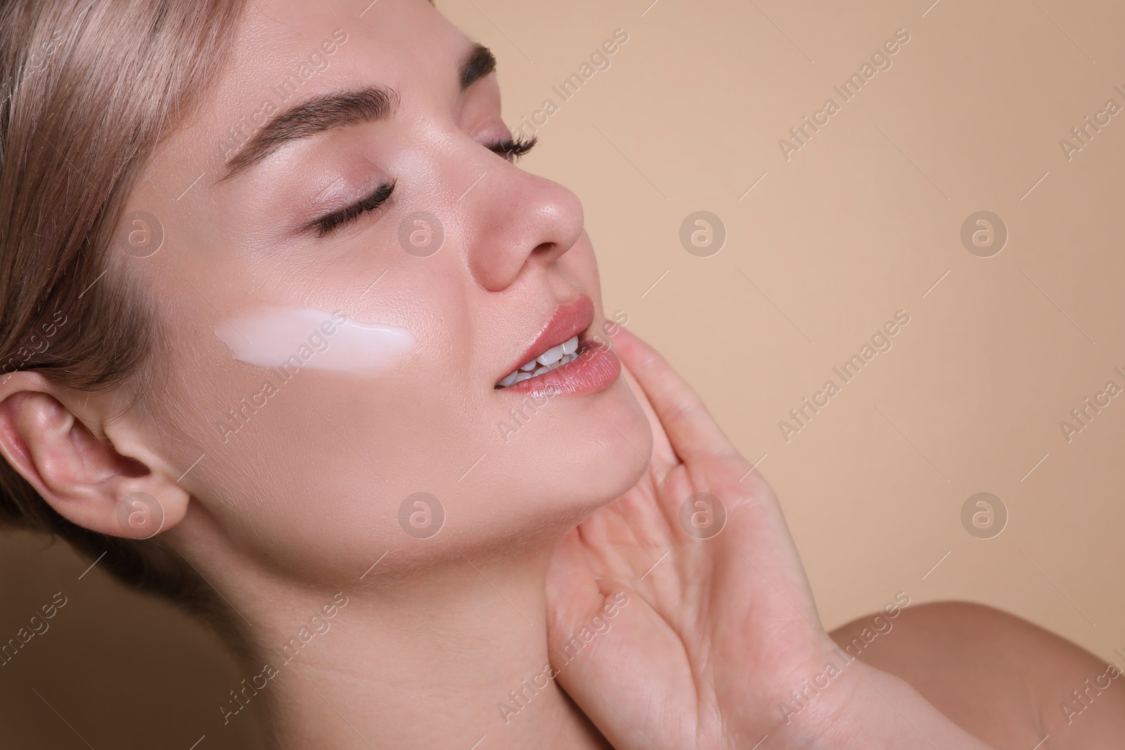 Photo of Beautiful woman with cream on her face against beige background, closeup. Space for text