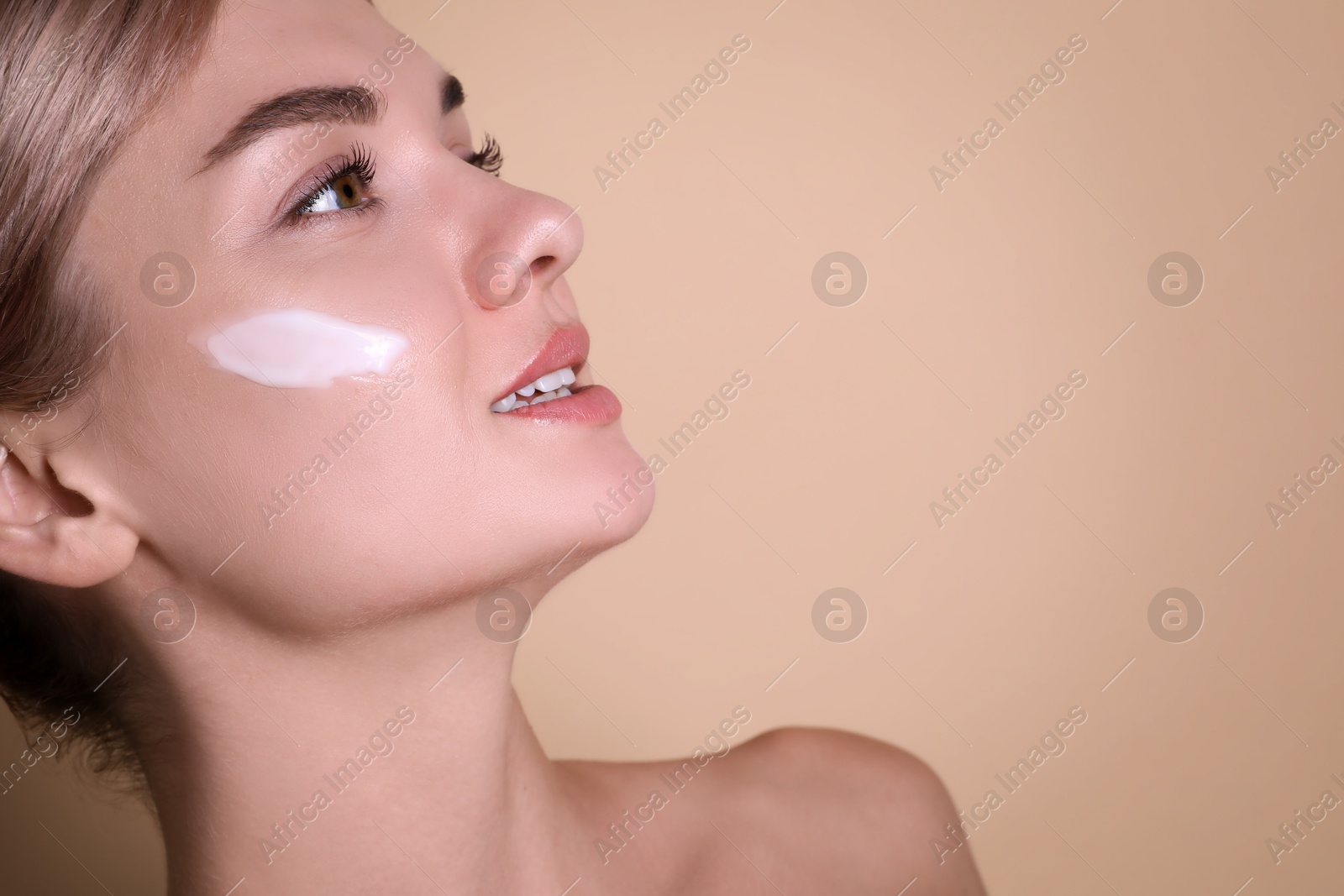 Photo of Beautiful woman with cream on her face against beige background, closeup. Space for text