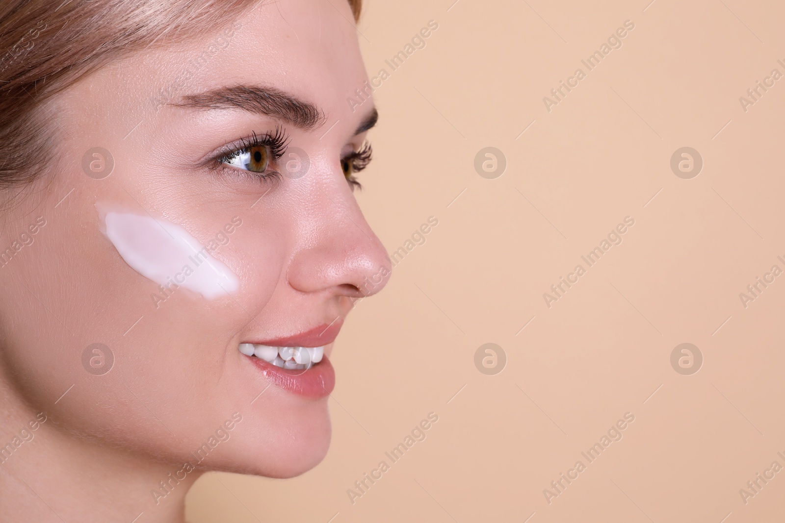 Photo of Beautiful woman with cream on her face against beige background, closeup. Space for text