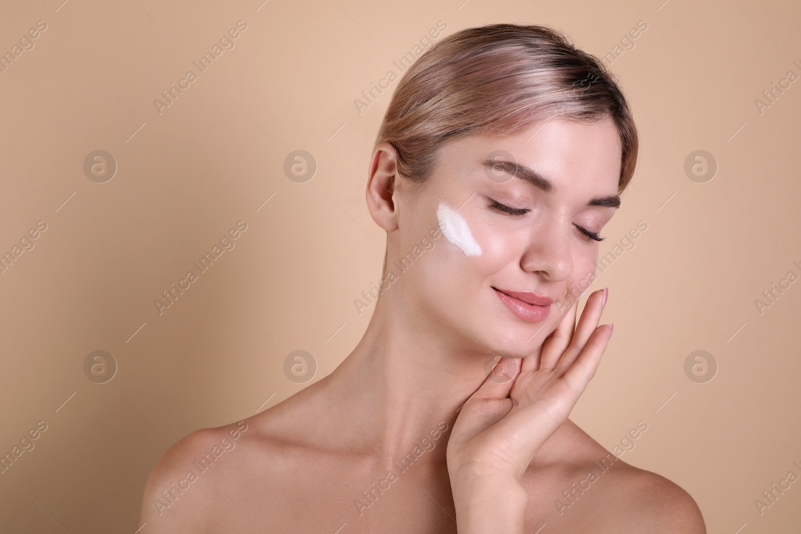 Photo of Beautiful woman with cream on her face against beige background, space for text