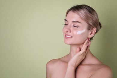 Photo of Beautiful woman with cream on her face against light green background, space for text