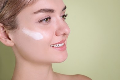 Photo of Beautiful woman with cream on her face against light green background, closeup. Space for text