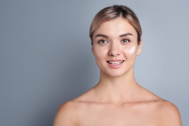 Photo of Beautiful woman with cream on her face against gray background