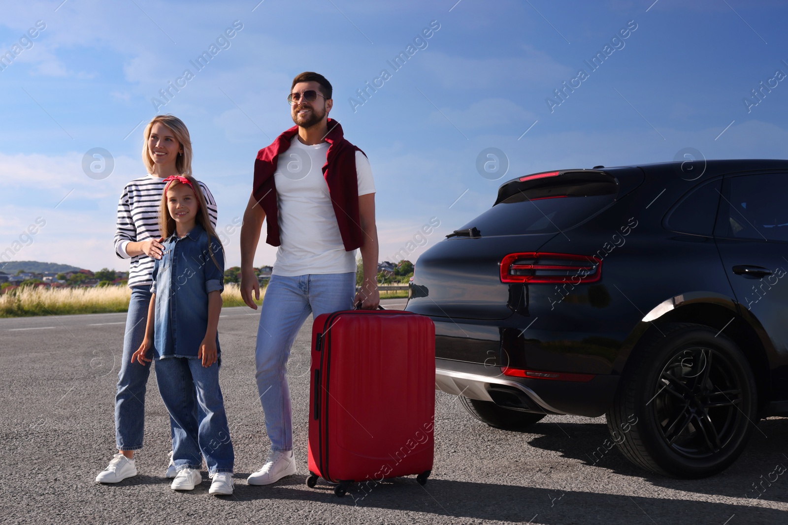 Photo of Happy family with red suitcase near car outdoors