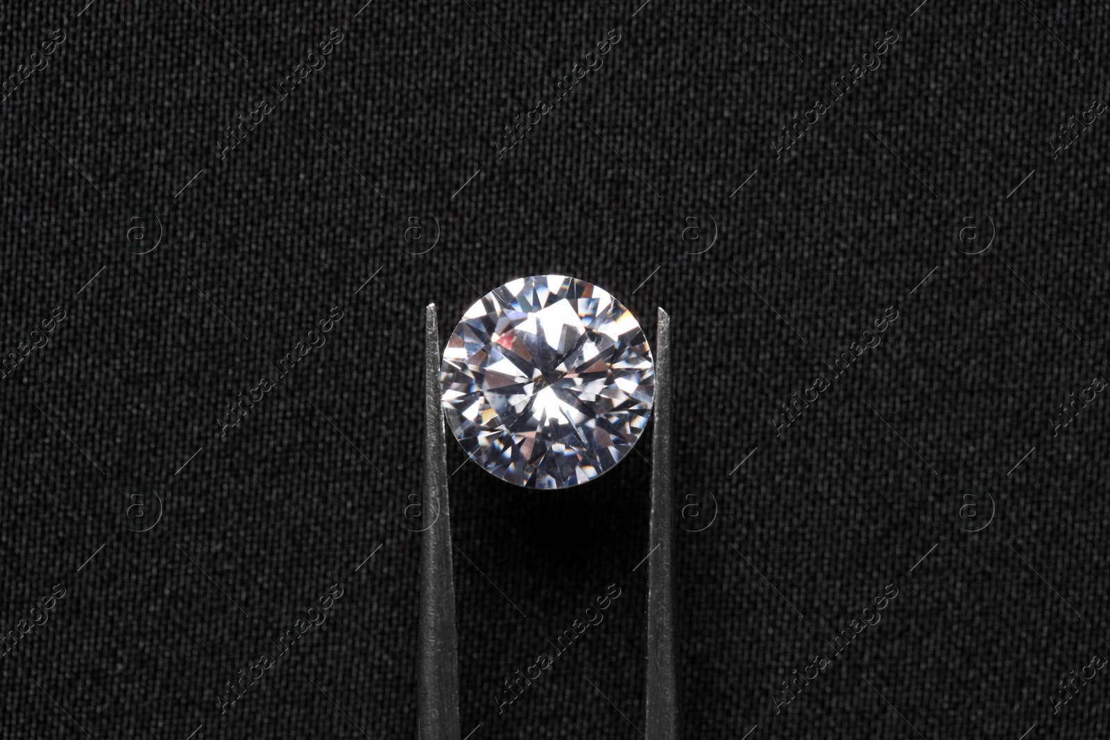 Photo of Tweezers with beautiful shiny diamond on black fabric, top view