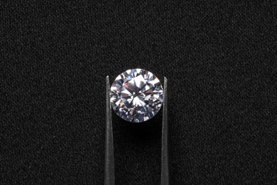 Photo of Tweezers with beautiful shiny diamond on black fabric, top view