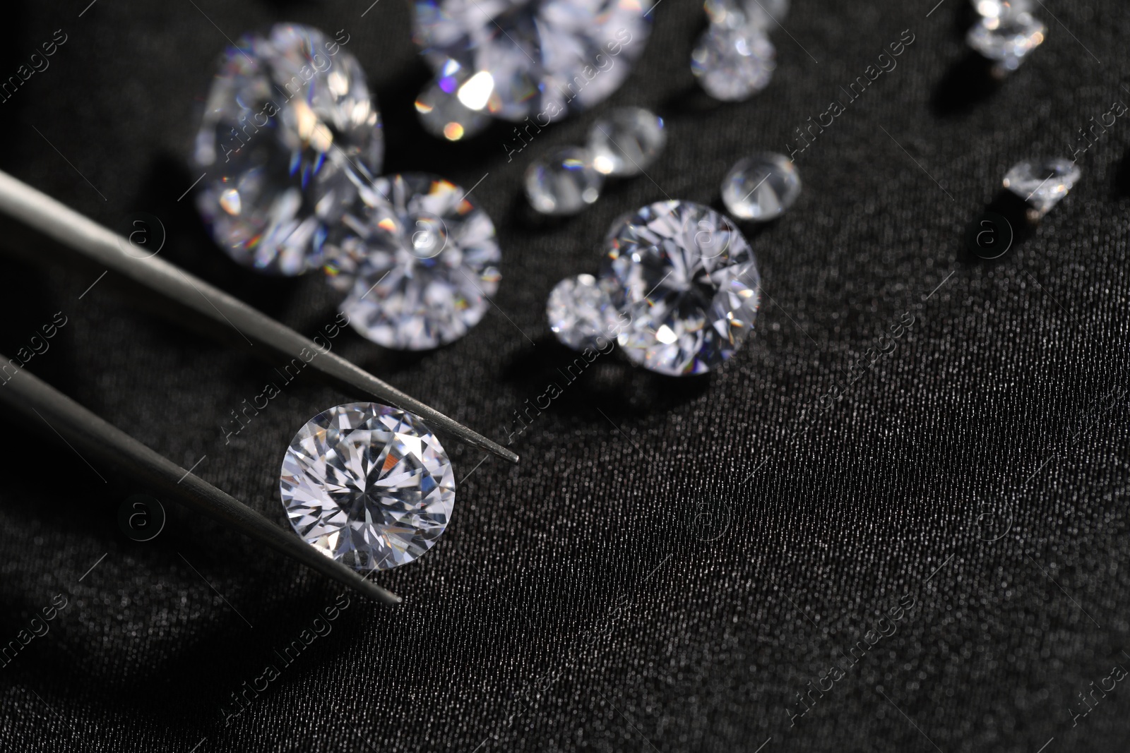 Photo of Tweezers with beautiful shiny diamonds on black fabric, closeup