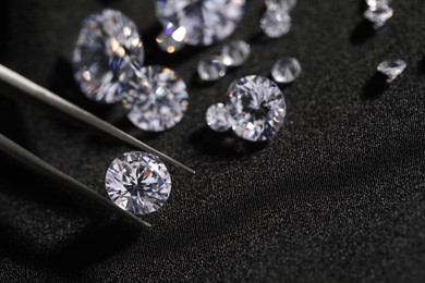 Photo of Tweezers with beautiful shiny diamonds on black fabric, closeup