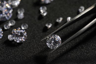 Tweezers with beautiful shiny diamonds on black fabric, closeup