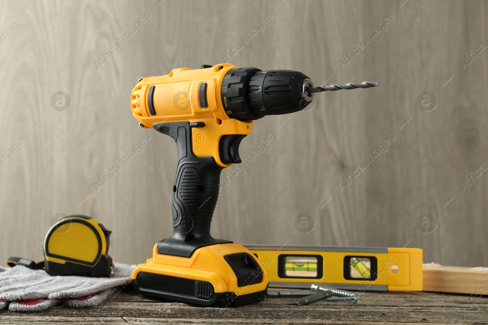 Photo of Cordless electric drill, gloves, bits, measuring tape and building level on wooden table