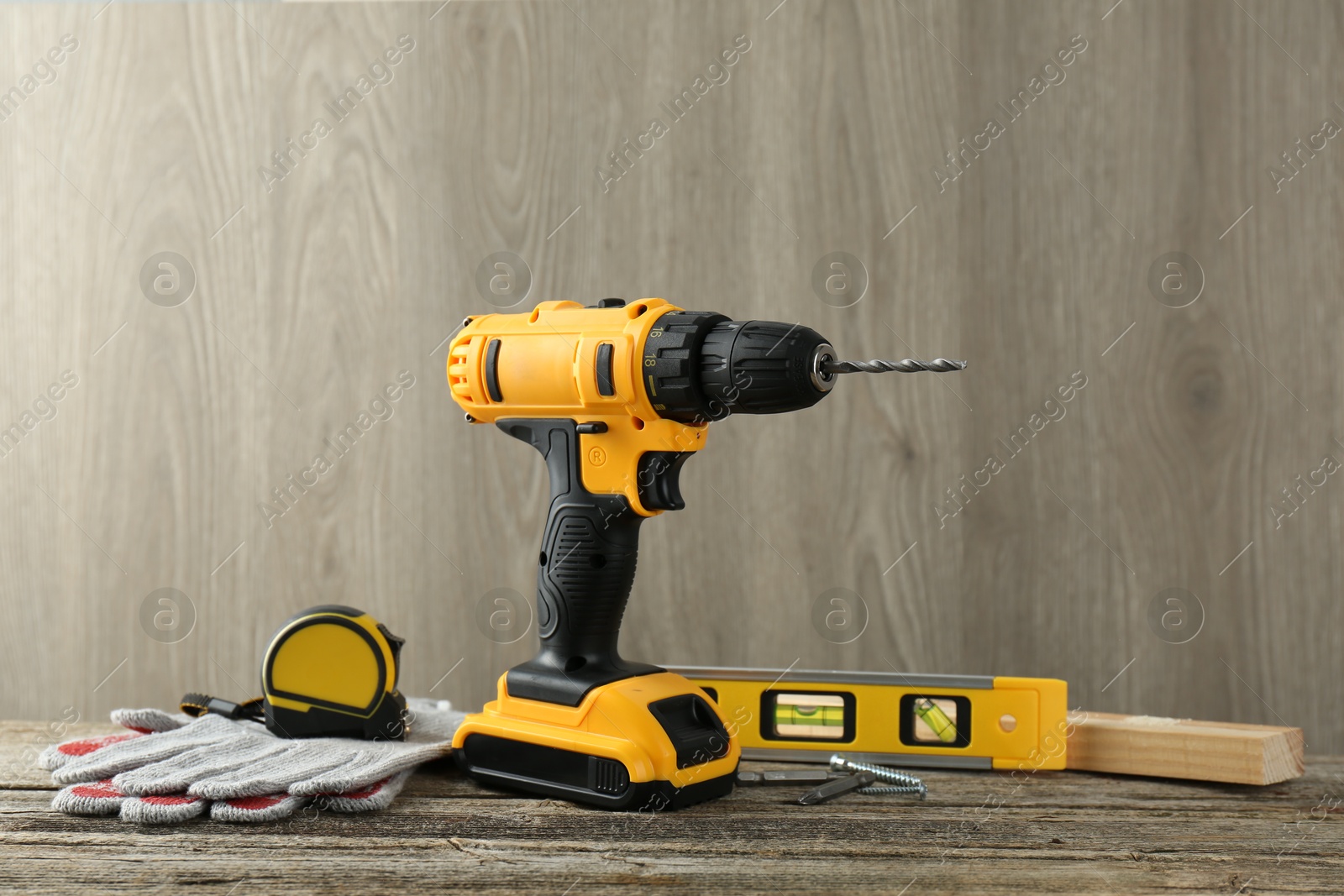 Photo of Cordless electric drill, gloves, bits, measuring tape and building level on wooden table