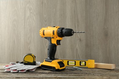 Photo of Cordless electric drill, gloves, bits, measuring tape and building level on wooden table