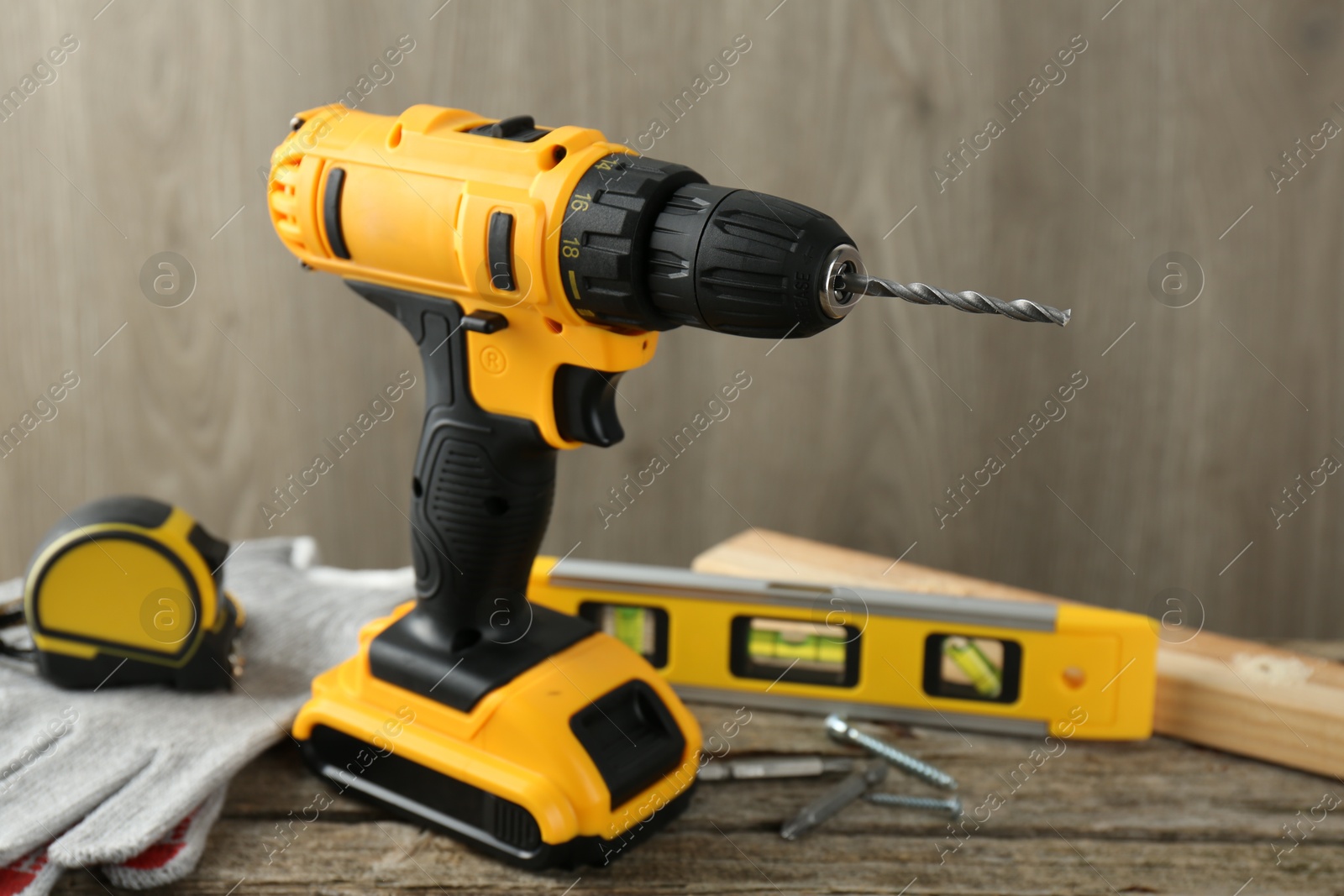 Photo of Cordless electric drill, gloves, bits, measuring tape and building level on wooden table