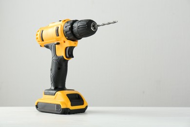 Photo of One cordless electric drill on white wooden table, space for text