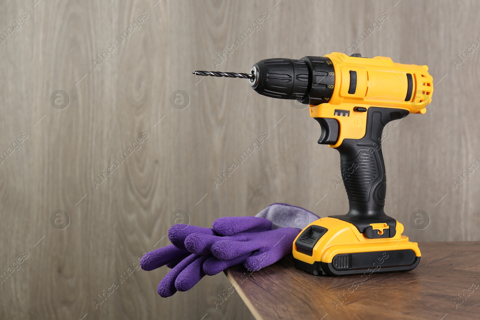 Photo of Cordless electric drill and gloves on wooden table, space for text