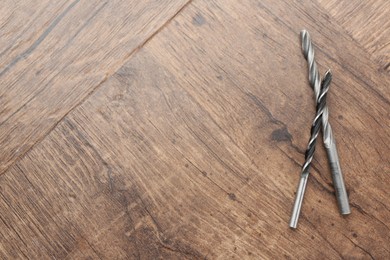 Photo of Two drill bits on wooden surface, top view. Space for text