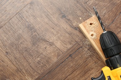 Photo of Cordless electric drill, plank and sawdust on wooden table, top view. Space for text