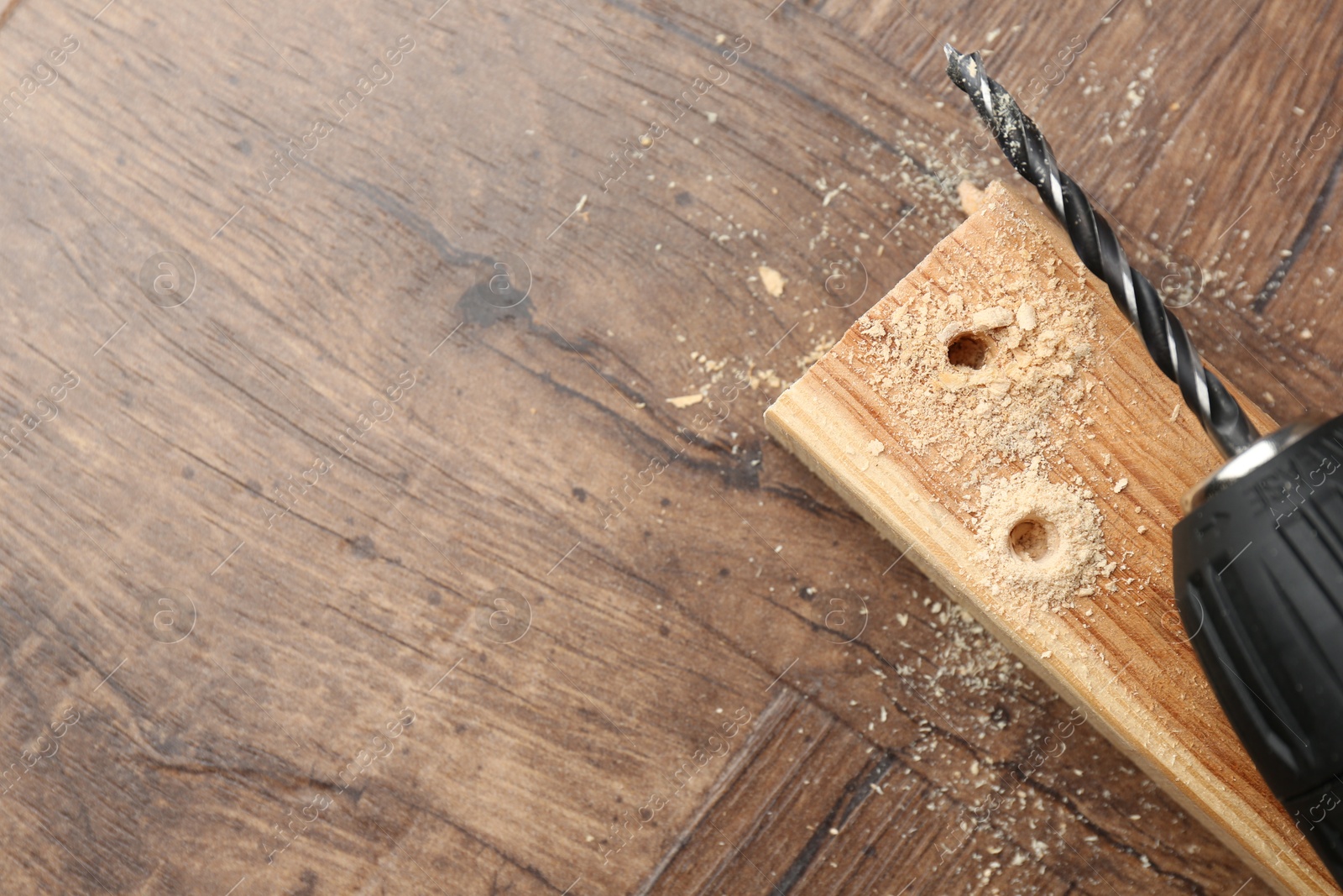 Photo of Cordless electric drill, plank and sawdust on wooden table, top view. Space for text