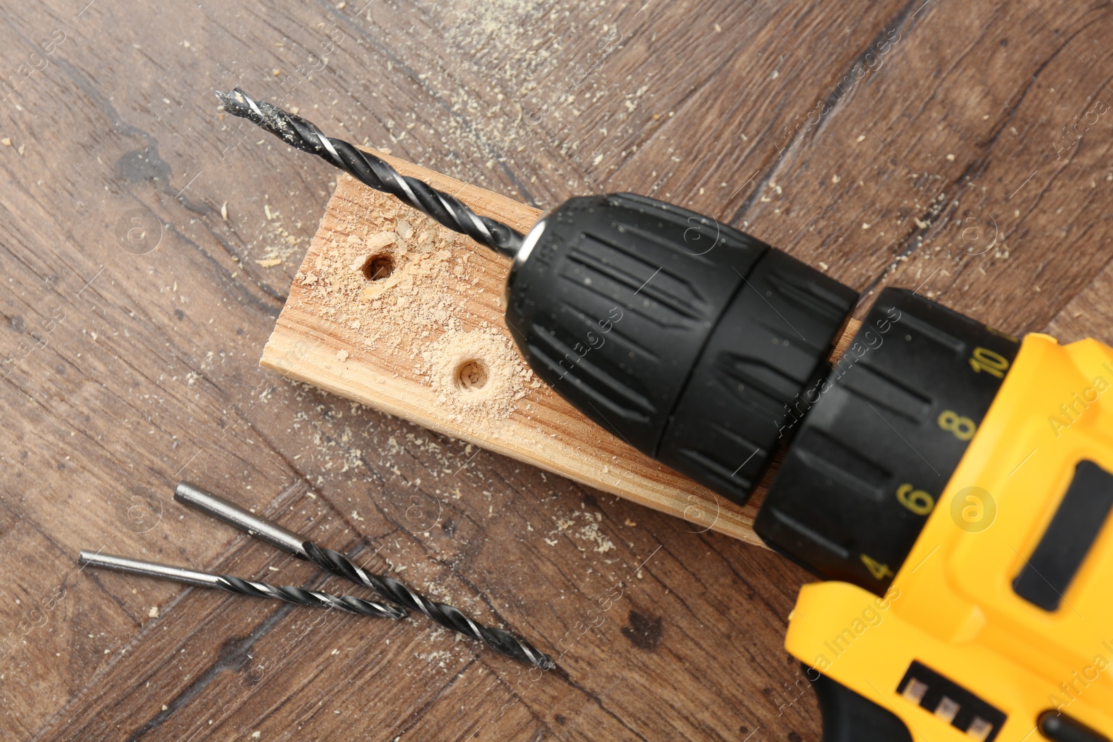 Photo of Cordless electric drill, bits, plank and sawdust on wooden table, top view