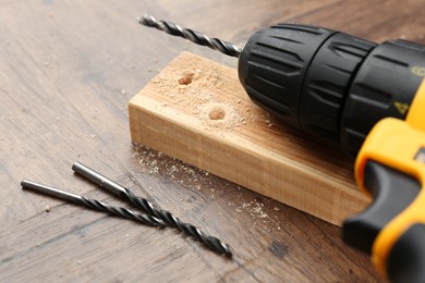 Photo of Cordless electric drill, bits, plank and sawdust on wooden table, closeup