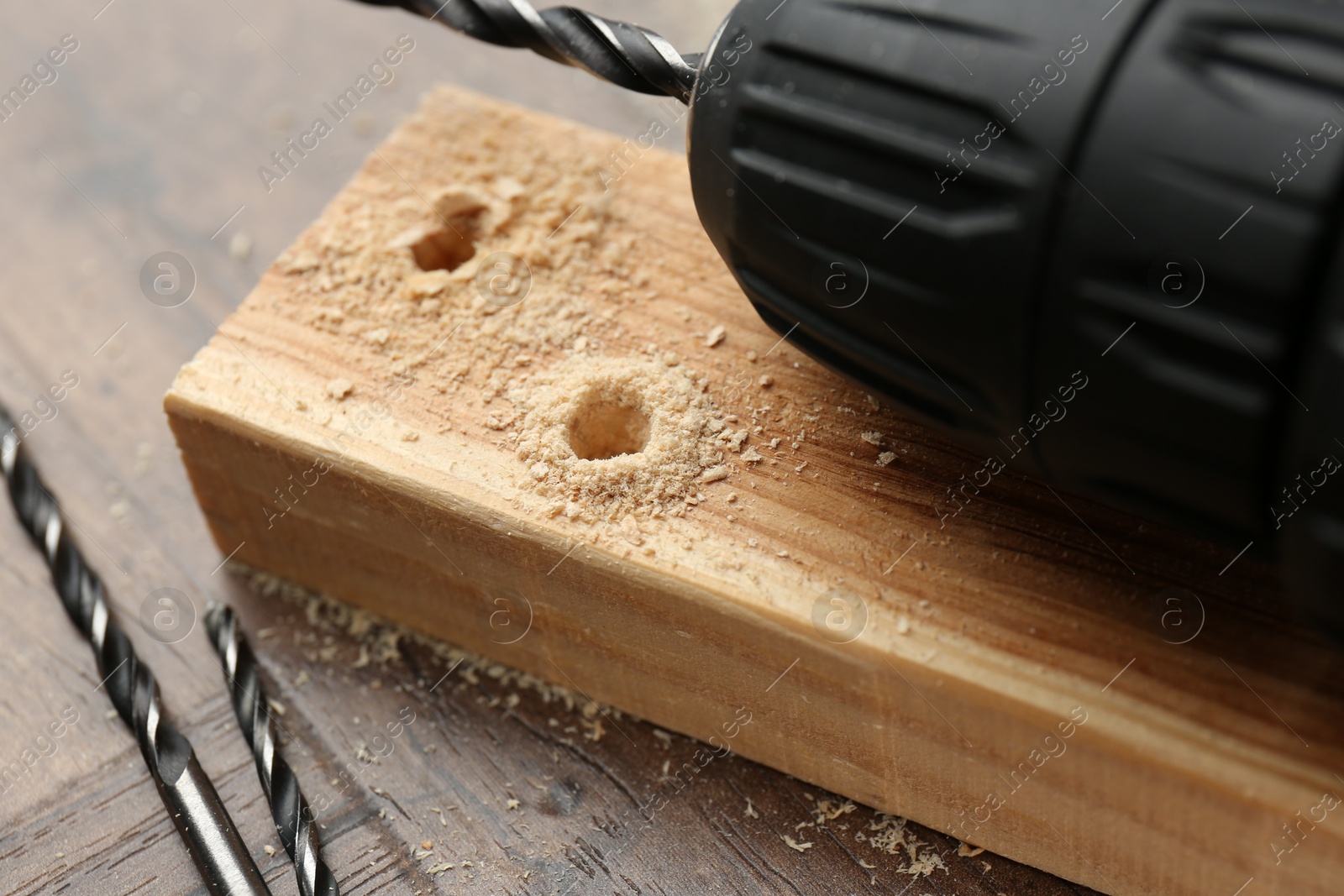 Photo of Cordless electric drill, bits, plank and sawdust on wooden table, closeup