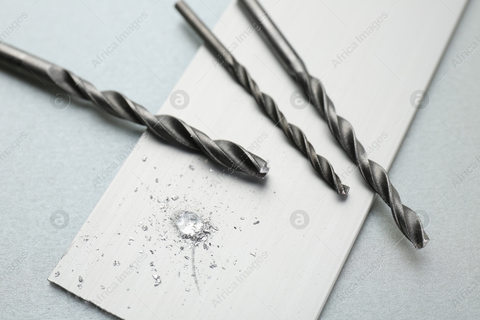 Photo of Drill bits, plank and sawdust on light grey background