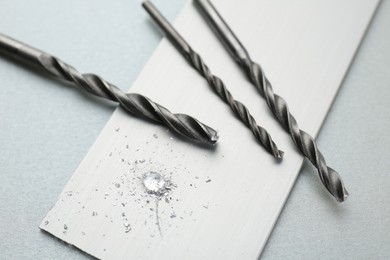 Drill bits, plank and sawdust on light grey background