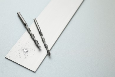 Photo of Drill bits, plank and sawdust on light grey background, space for text