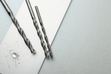 Photo of Drill bits, plank and sawdust on light grey background, top view. Space for text