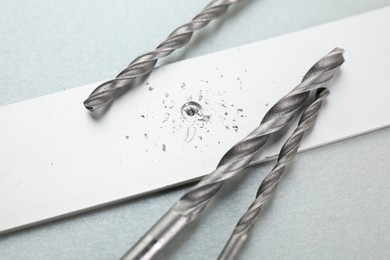 Photo of Drill bits, plank and sawdust on light grey background, closeup