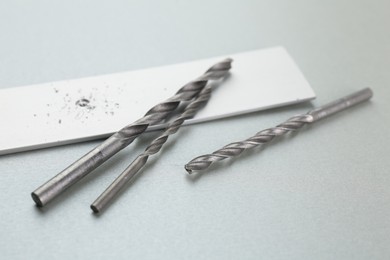 Photo of Drill bits, plank and sawdust on light grey background