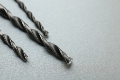 Different drill bits on light grey background, closeup. Space for text