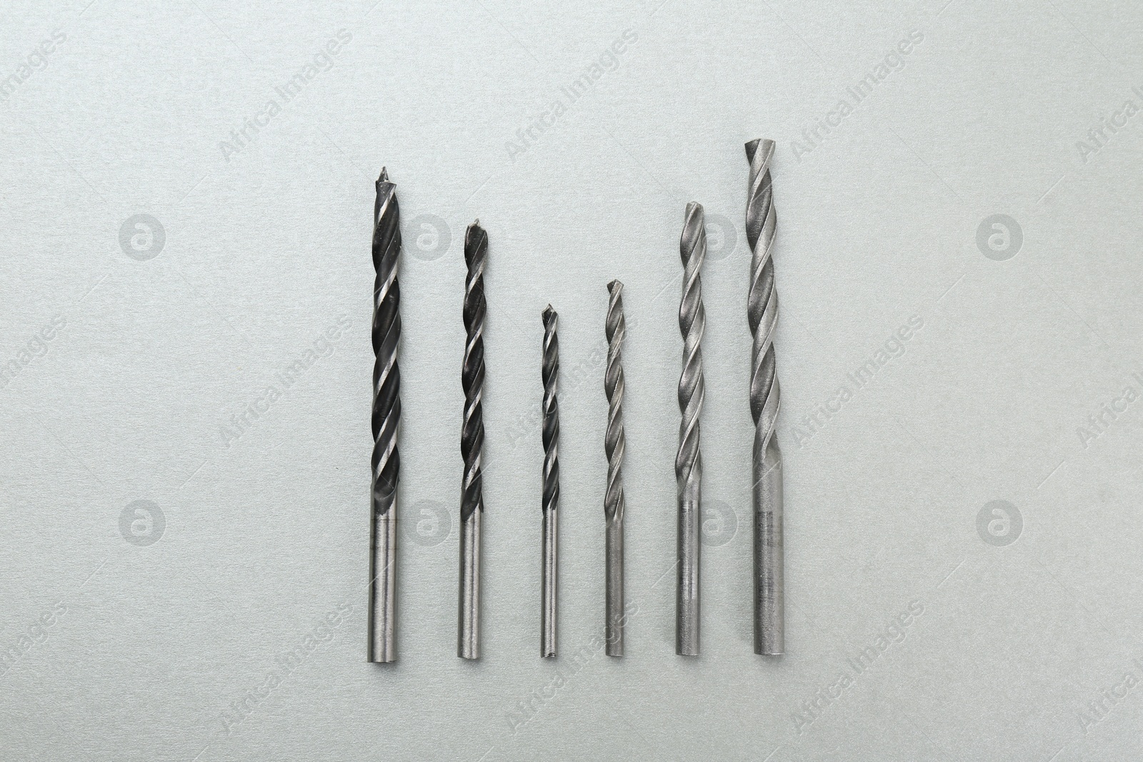 Photo of Many different drill bits on light grey background, top view