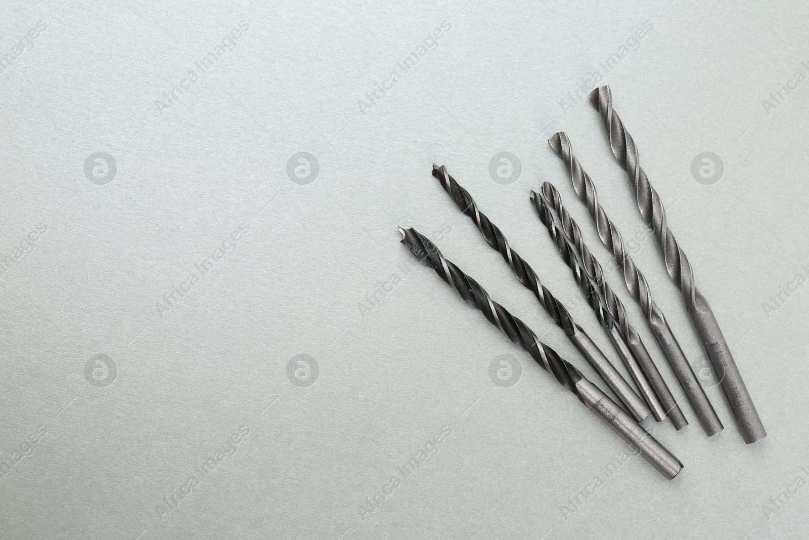 Photo of Many different drill bits on light grey background, top view. Space for text