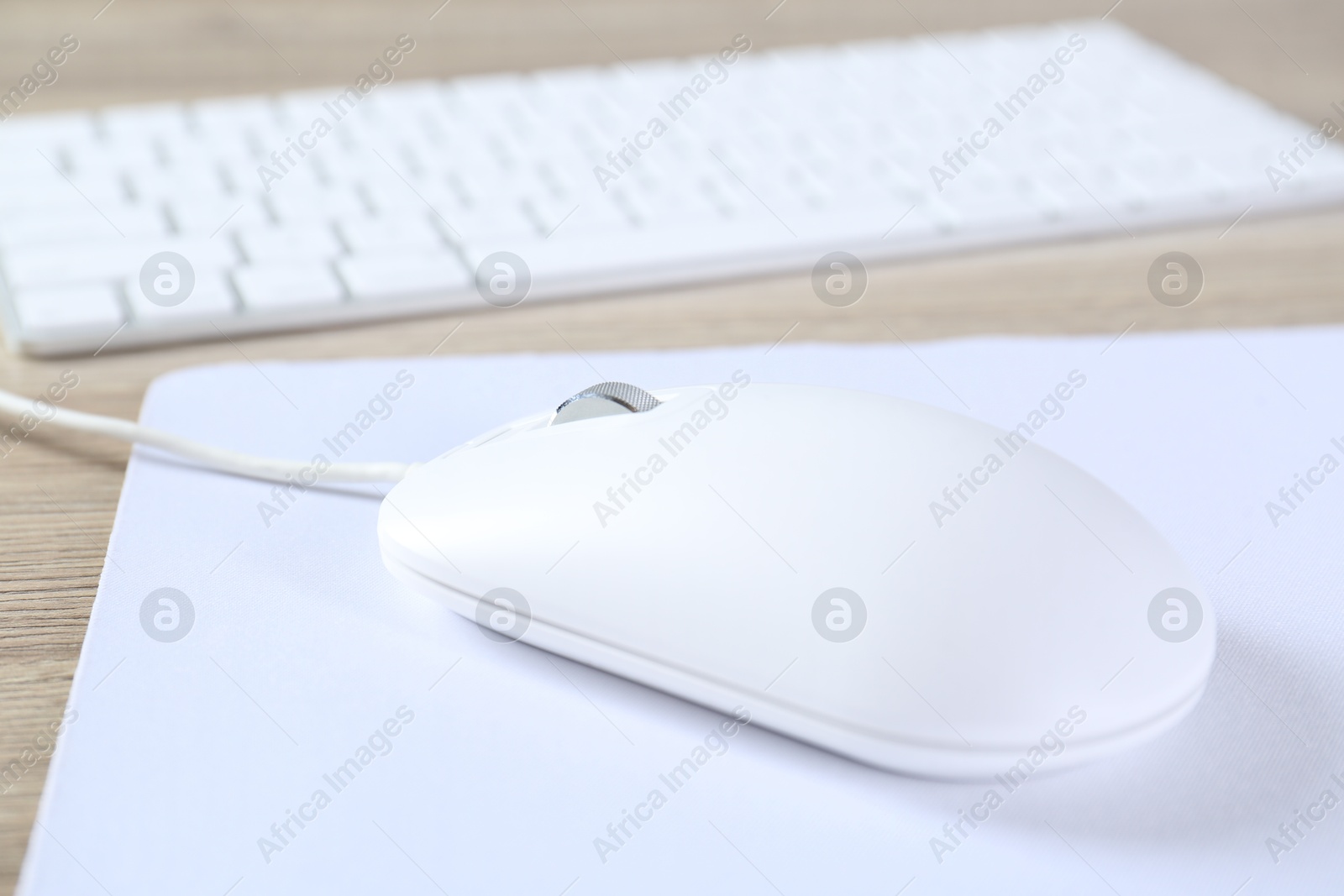 Photo of White computer mouse with mousepad and keyboard on wooden table, closeup