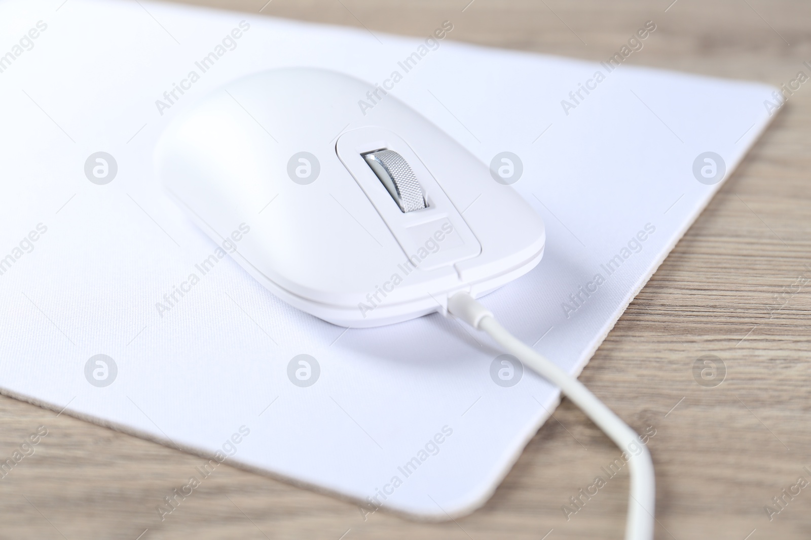 Photo of White computer mouse and mousepad on wooden table, closeup