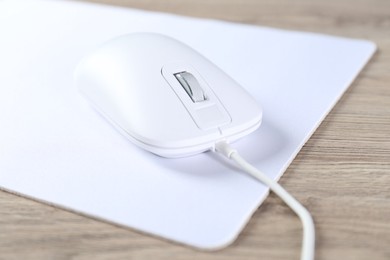 Photo of White computer mouse and mousepad on wooden table, closeup