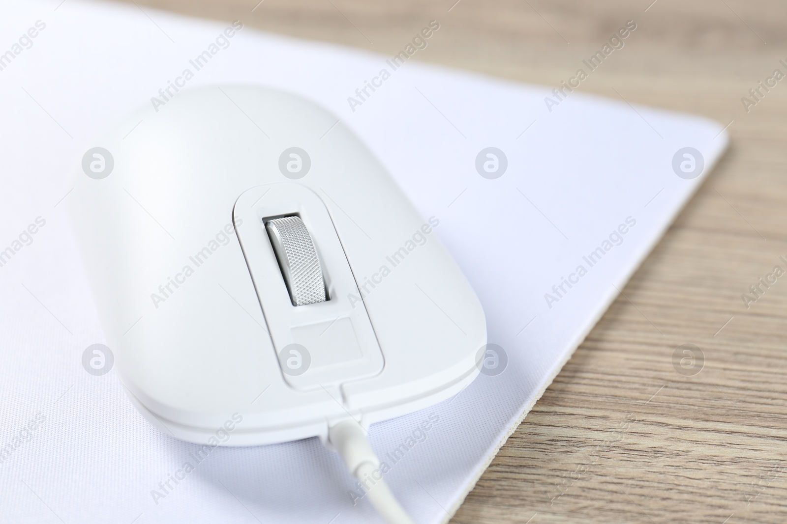 Photo of White computer mouse and mousepad on wooden table, closeup