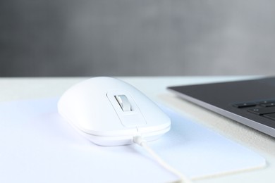 Photo of Computer mouse with mousepad and laptop on white table, closeup