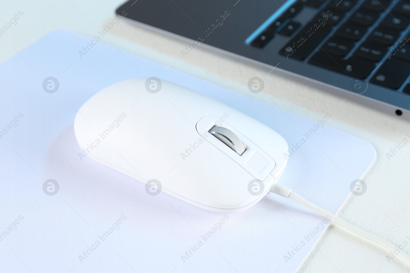 Photo of Computer mouse with mousepad and laptop on white table, closeup