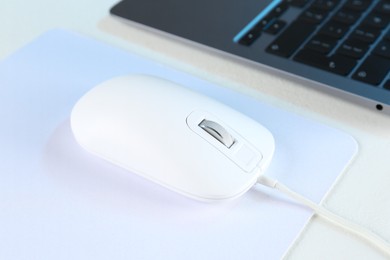 Photo of Computer mouse with mousepad and laptop on white table, closeup