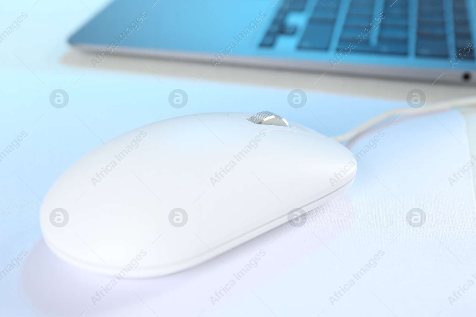 Photo of Computer mouse with mousepad and laptop on white table, closeup