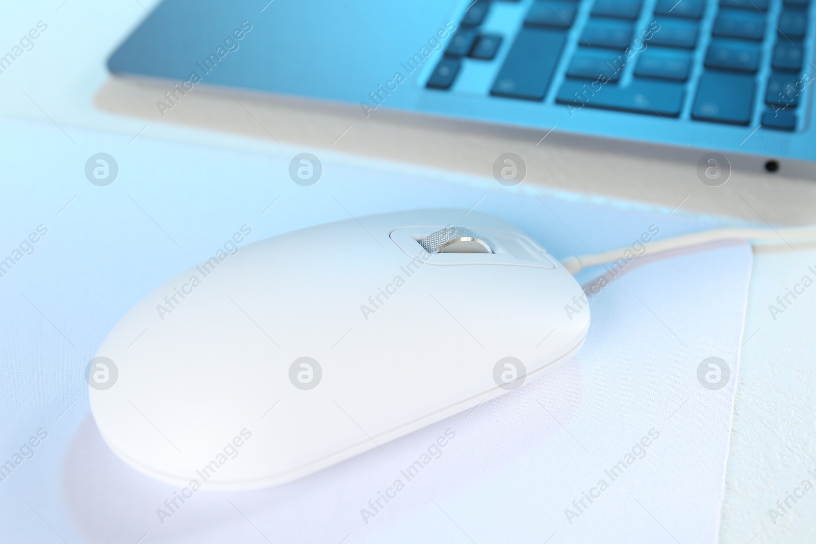 Photo of Computer mouse with mousepad and laptop on white table, closeup