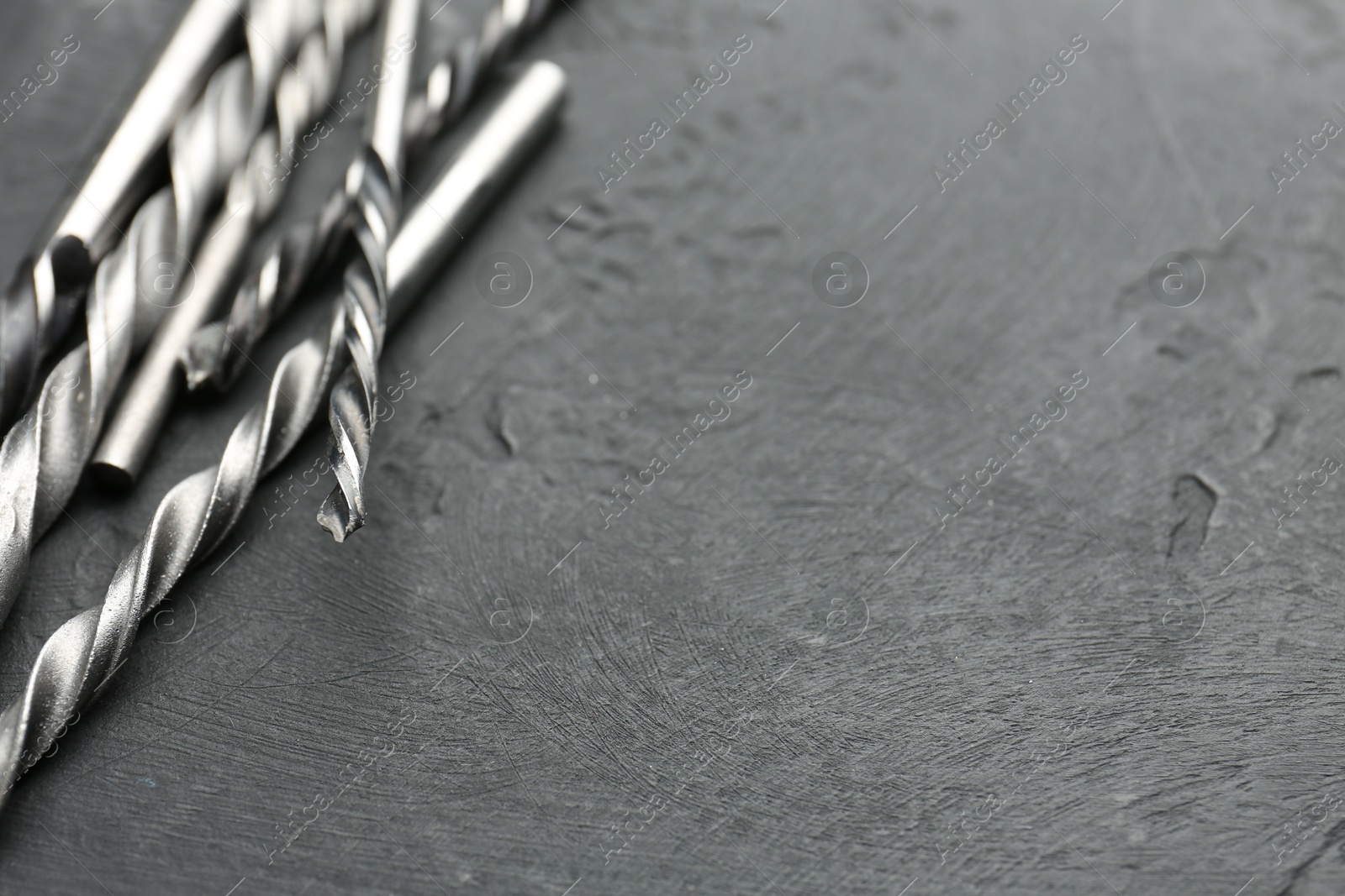 Photo of Many different drill bits on grey table, closeup. Space for text