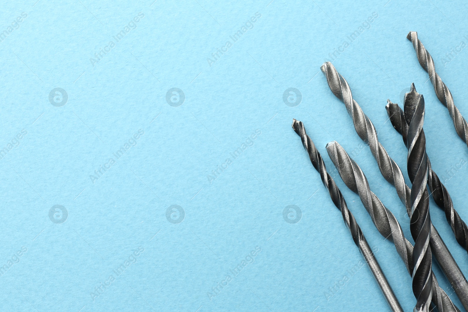 Photo of Many different drill bits on light blue background, top view. Space for text